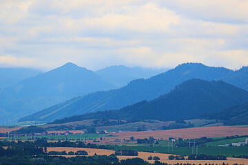 A vast mountainous landscape with layers of blue and green hills leading to distant peaks under a cloudy sky.