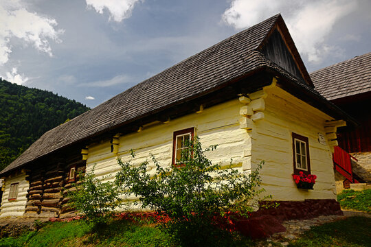 A charming traditional Slovak wooden log house with a prominent roof, set against a green hillside.