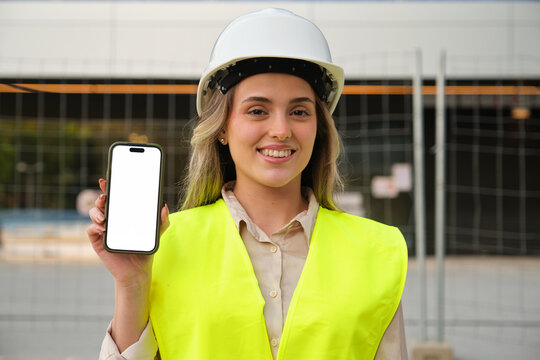 Confident construction engineer showing smartphone with blank screen for advertisement at building site