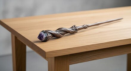 Intricately carved wooden wand with amethyst tip rests on light oak table.