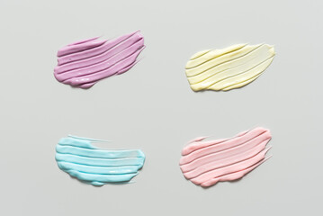Colored smears of cosmetic cream on gray pastel background, colorful cream samples with striped pattern, cosmetic banner, top view