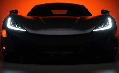 Sleek black sports car positioned against vibrant orange background. Headlights, rear lights glowing, creating striking contrast. Angled slightly to left, ready to navigate road course. Luxury