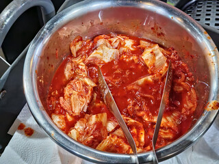 a bowl of kimchi with metal tongs rest inside the container