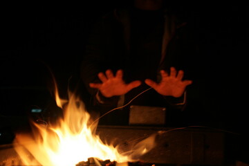 Fototapeta premium Warm glow of flames dances in the night as hands reach out for comfort and connection by the fire