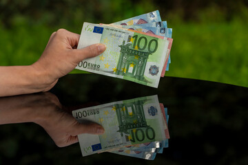 Hand holding various euro banknotes with clear reflection on glass surface, symbolizing financial stability, currency strength, investment, and wealth management. Green background 