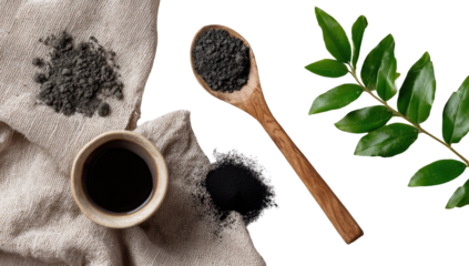 Dark powder, wooden spoon, and leaves on cloth. A cup of liquid