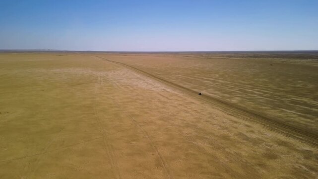The car is driven across the dried seabed of the vanishing Aral Sea, once one of the largest lakes in the world. Numerous vehicle tracks crisscross the salt-covered surface.