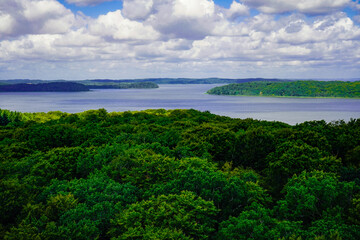 View over dense green forest to the small Jasmund Bodden with a cloudy sky and distant islands and headlands. The view over the trees, 18609 Binz on the island of Rügen