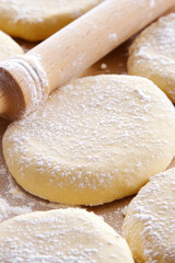 Dough circles dusted with flour are placed next to a wooden rolling pin. Baking preparation, dough, rolling pin