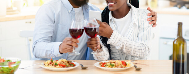 Millennial Couple's Lifestyle. Young Black Lovers Taking Photos On Smartphone While Having Date At Home, Happy African American Couple Drinking Red Wine And Enjoying Tasty Spaghetti, Free Space