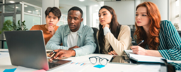 Creative international business team brainstorming at group meeting and thinking of new project, four mixed race pensive colleagues sitting at table using laptop together, start up concept
