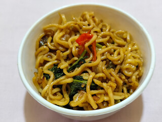 Chewy instant fried noodles in a white bowl, highlighting its texture and deliciousness, against a blurry bowl background.