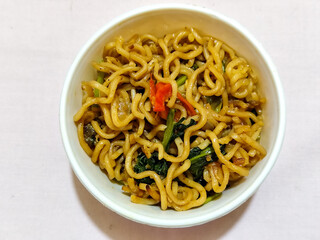 Chewy instant fried noodles in a white bowl, highlighting its texture and deliciousness, against a blurry bowl background.