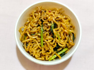 Chewy instant fried noodles in a white bowl, highlighting its texture and deliciousness, against a blurry bowl background.