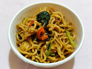 Chewy instant fried noodles in a white bowl, highlighting its texture and deliciousness, against a blurry bowl background.