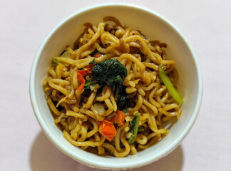 Chewy instant fried noodles in a white bowl, highlighting its texture and deliciousness, against a blurry bowl background.