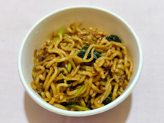 Chewy instant fried noodles in a white bowl, highlighting its texture and deliciousness, against a blurry bowl background.