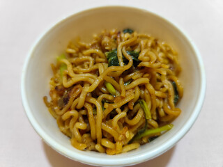 Chewy instant fried noodles in a white bowl, highlighting its texture and deliciousness, against a blurry bowl background.