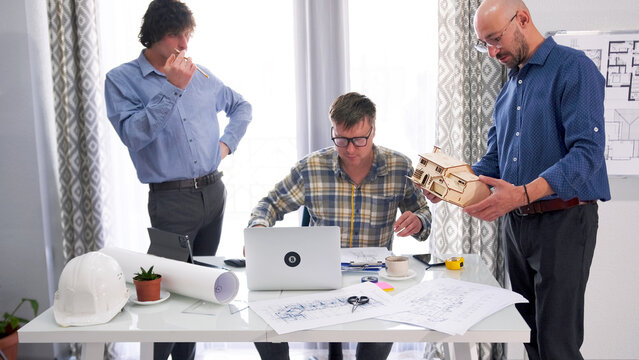 Three men are working on a country house project. A designer, architect and engineer create ideas for a smart home