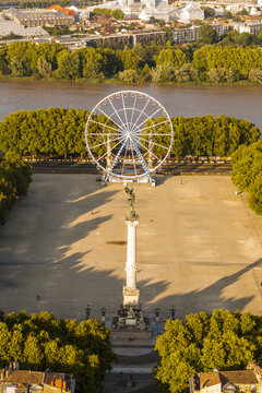 Aerial view of the Place des Quinconces with its iconic Ferris wheel and monument casting long shadows in the sunlight, Bordeaux, France.