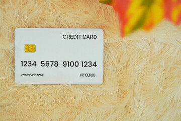 flat lay image of a white credit card, placed on a yellow fur and orange leaf in foreground. financial technology concept
