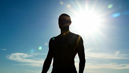Man silhouette with arms raised against bright sun rays creating dramatic backlit portrait. Inspiration concept for motivational content, fitness programs and personal achievement campaigns