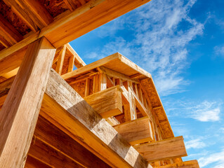 Upward view of a wooden house under construction against a blue sky