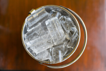 A silver bucket with ice cubes on wood table. Top view