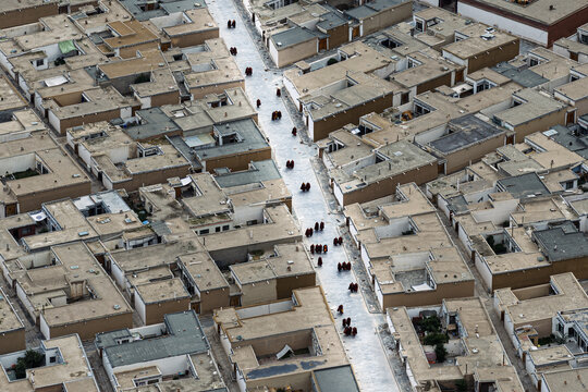 Aerial view of the Labrang Monastery nestled within the town, a tapestry of rooftops and narrow streets against the backdrop of rolling green hills, Xiahe County, China.