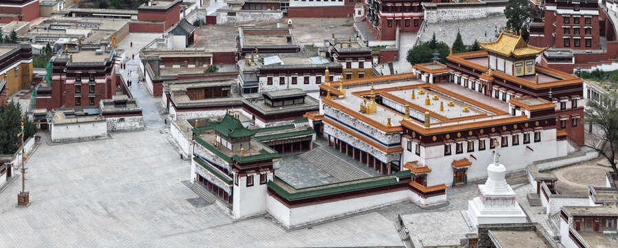 Aerial view of the monastery's golden roofs and red walls stand in stark contrast to the expansive gray stone courtyard, Xiahe County, China.