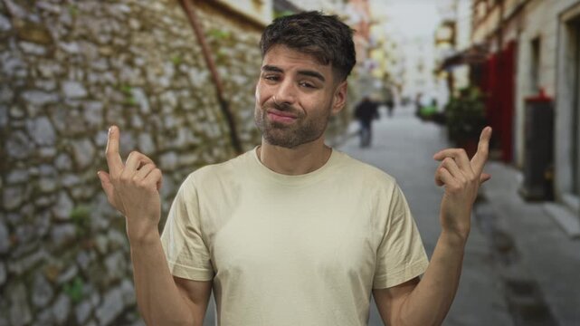 Young man finger pointing to chest in narrow street with stone wall and blurred pedestrians; uncertainty doubt hesitation confusion.