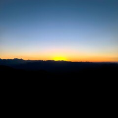Sunrise over dark mountain range, with a gradient sky from blue to orange.