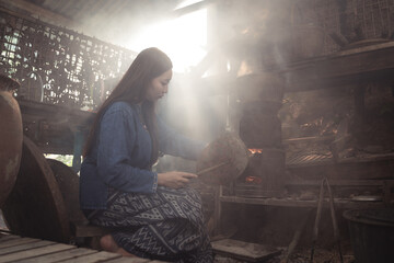 A dramatic silhouette of a young woman cooking, framed by intense backlighting and thick, swirling smoke. This atmospheric image creates a mysterious and timeless mood of rural life.