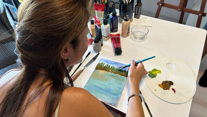 A close-up of a female painter demonstrating her craftsmanship as she works on a canvas with various colors of paint and brushes