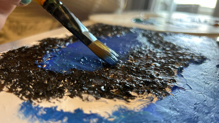 A close-up of a female painter demonstrating her craftsmanship as she works on a canvas with various colors of paint and brushes