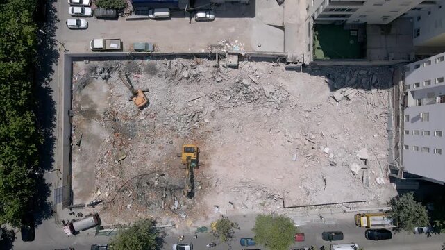 Aerial view of excavators clearing debris at a demolition site. Construction machinery working among broken concrete, bricks, and metal as the area is prepared for new building development. 