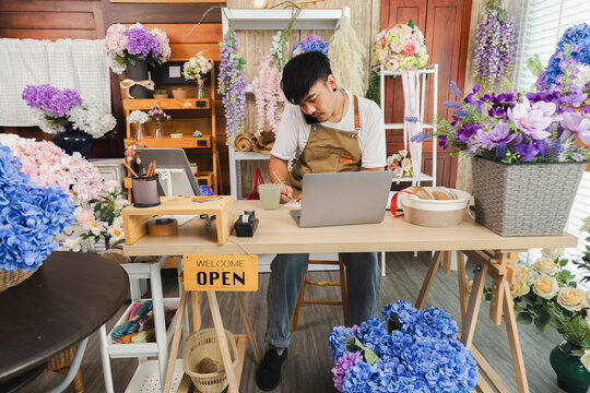 Small business, florist shop owner, flower man lifestyle managing phone call order from customer while tying ribbon, Asian florist entrepreneur multitasks at shop, male using smartphone technology - Powered by Adobe