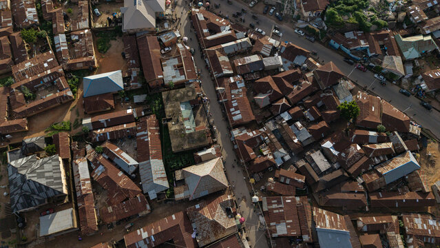 Aerial view of tightly packed buildings with rusty rooftops reflecting the sunlight next to a busy street bustling with vehicles, Jos, Plateau, Nigeria.