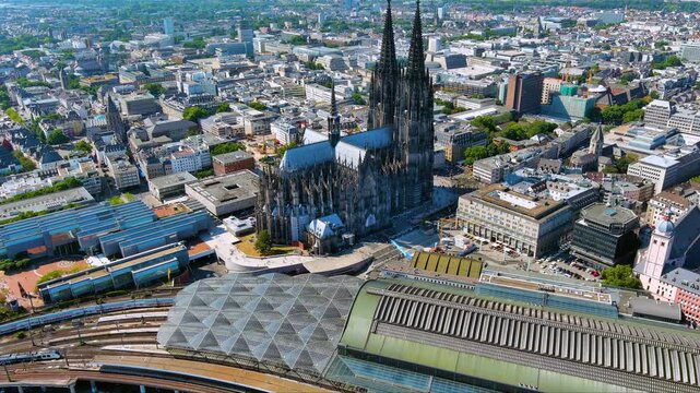 4K drone view of Cologne Cathedral and Hauptbahnhof - twin spires dominating the city center. Gothic UNESCO icon framed by rail tracks and modern roofs over bustling Cologne Germany.