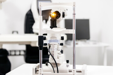 Ophthalmic examination equipment featuring a slit lamp with illuminated lens, positioned on a clinical table in a modern eye care facility