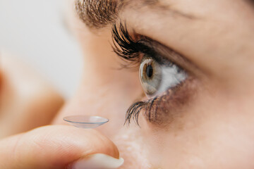 Close-up of a woman applying a contact lens to her eye, showcasing the delicate process of lens insertion, with focus on the eye's intricate details and the lens's clarity and texture