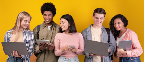 Modern devices for education, generation z and social media for study and chatting. Cheerful young multiracial people learning, using digital gadgets, isolated on orange background, copy space © Prostock-studio