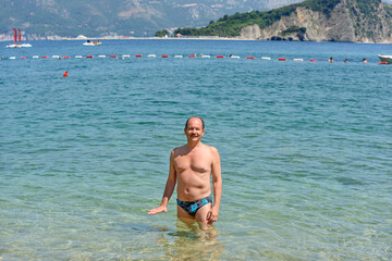 Man is standing  in water of Mogren beach, Budva, Montenegro.