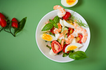 Diet dish with shrimps, tomatoes and boiled eggs on a green background