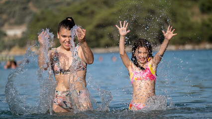 Fototapeta premium The sisters having fun together playing and splashing water in the sea during vacation