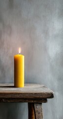 Single yellow candle on weathered wooden stool against textured wall