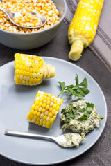 Pieces of boiled corn, sauce and spoon on gray plate.