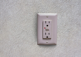 Electrical wall outlet with ground fault circuit interrupter (GFCI) showing reset and test buttons on textured white wall background.