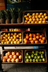 Fresh fruits in wooden crates outside a store: pineapples, lemons, oranges, grapefruits, and green apples.