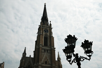 Tall bell tower of Name of Mary Church in Novi Sad, Serbia. Beautiful Gothic-style detail under a dramatic cloudy sky.